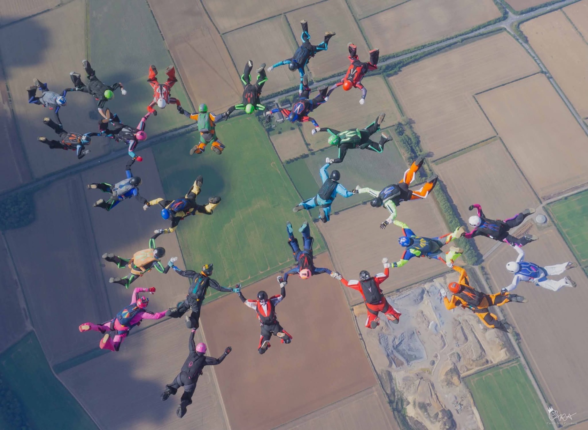 A formation of skydivers seen from above over farmland